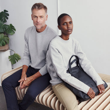 a man and a woman sitting on a bench wearing matching grey sweaters with a plant in the background.