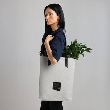 a female model carries a white tote bag with black straps, filled with greenery