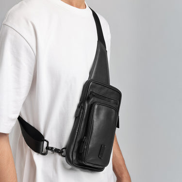 Person wearing a black leather sling bag on a plain background